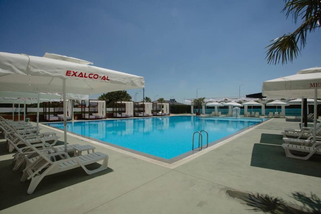 Piscina com espreguiçadeiras e guarda-sóis identificados com 'EXALCO-AI' e 'MEXALCO-AI'.