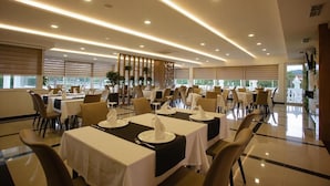 Un'ampia sala da pranzo con numerosi tavoli apparecchiati per il servizio, ampie finestre e un moderno design del soffitto.