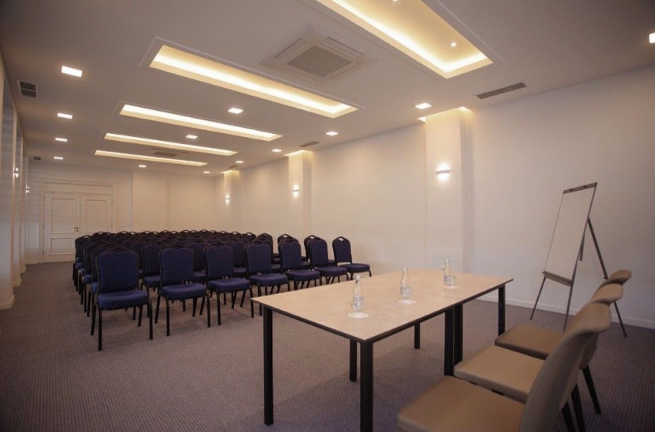 Una sala conferenze con file di sedie, un tavolo con bottiglie d'acqua e un supporto per lavagna.