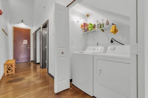 A laundry area with a washing machine and dryer, a wooden stool, and a shelf with various bottles and containers. - Cozy mill loft w/ 2 king beds, gym & pool (Arcadia)
