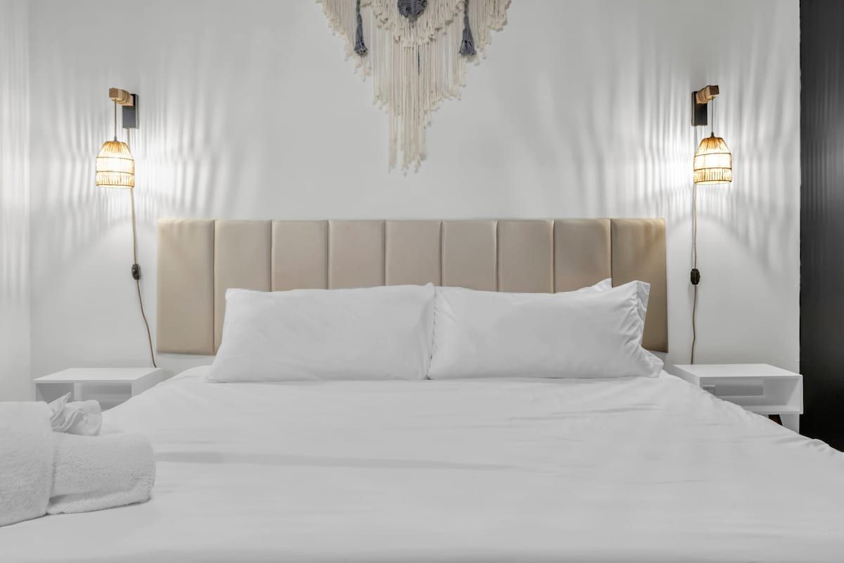 A hotel room with a large bed, two bedside tables, a wall-mounted light fixture, and a hanging decorative piece.