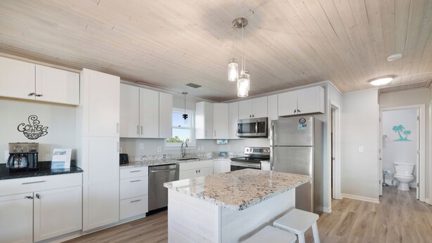 A modern kitchen with white cabinets, granite countertops, stainless steel appliances, and a wooden ceiling. - Beach Boyd's by Liquid Life (Gulf Shores)