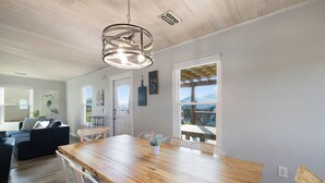 A spacious living area with a wooden dining table, a sofa, and a view of the outdoors. - Beach Boyd's by Liquid Life (Gulf Shores)