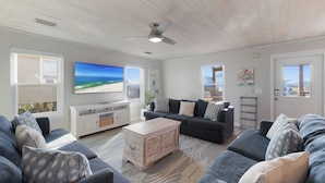 A spacious living room with a large gray sectional sofa, a white entertainment unit, and a ceiling fan. - Beach Boyd's by Liquid Life (Gulf Shores)
