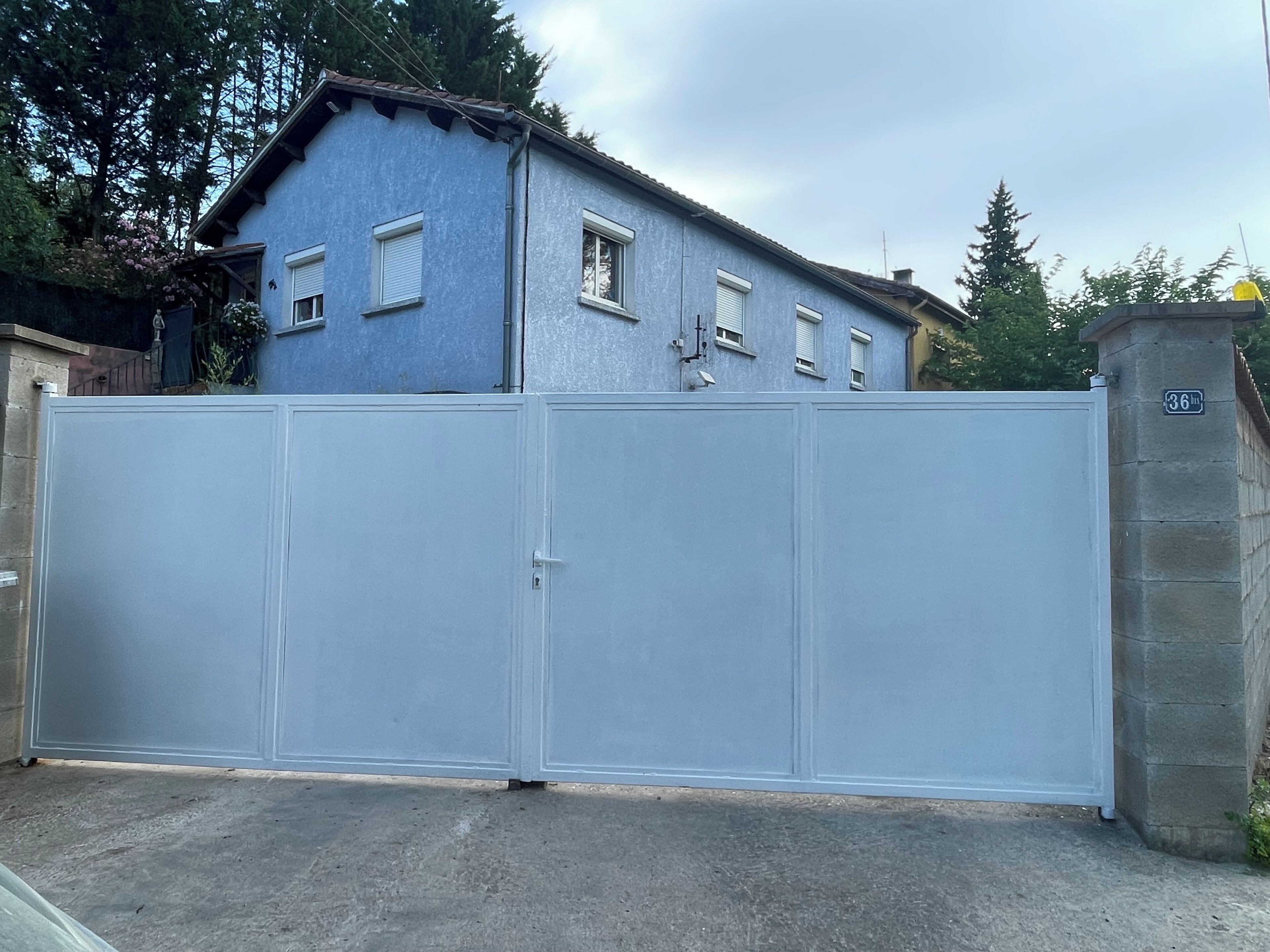 A gated residential area with a blue house, a white gate, and a stone wall with a sign.