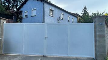 A gated residential area with a blue house, a white gate, and a stone wall with a sign.
