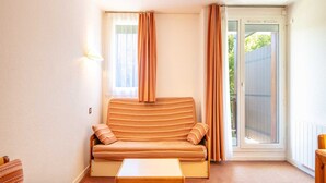 A room with a sofa, a table, and a sliding glass door leading to an outdoor area. - Mountain Apartment Near Village Centre (Villard-de-Lans)