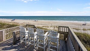 Un pontile in legno con poltrone Adirondack bianche che si affaccia su una spiaggia.