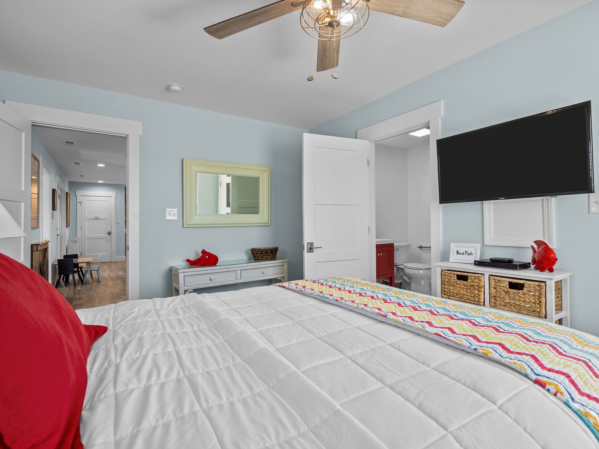 Ein Schlafzimmer mit Bett, Fernseher, Deckenventilator, Spiegel und einer Tür zu einem anderen Raum.