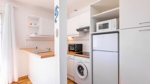 A compact kitchen with a washing machine, microwave, and a small countertop. - Le Repos Marin (Valras-Plage)