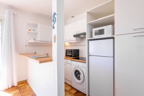 A compact kitchen with a washing machine, microwave, and a small countertop. - Le Repos Marin (Valras-Plage)