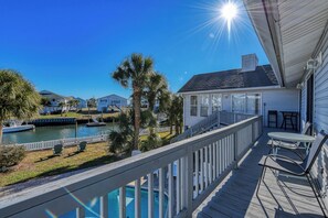 A wooden deck with a view of a body of water, a boat docked nearby, and a house with a balcony. - Five Bedroom Home with a Private Pool on the Channel and Pet Friendly (Garden City Beach)