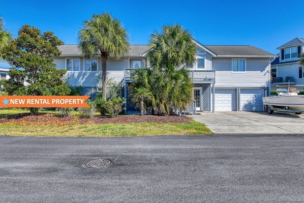 A two-story house with a garage, a boat in the driveway, and a sign indicating it's a new rental property. - Five Bedroom Home with a Private Pool on the Channel and Pet Friendly (Garden City Beach)