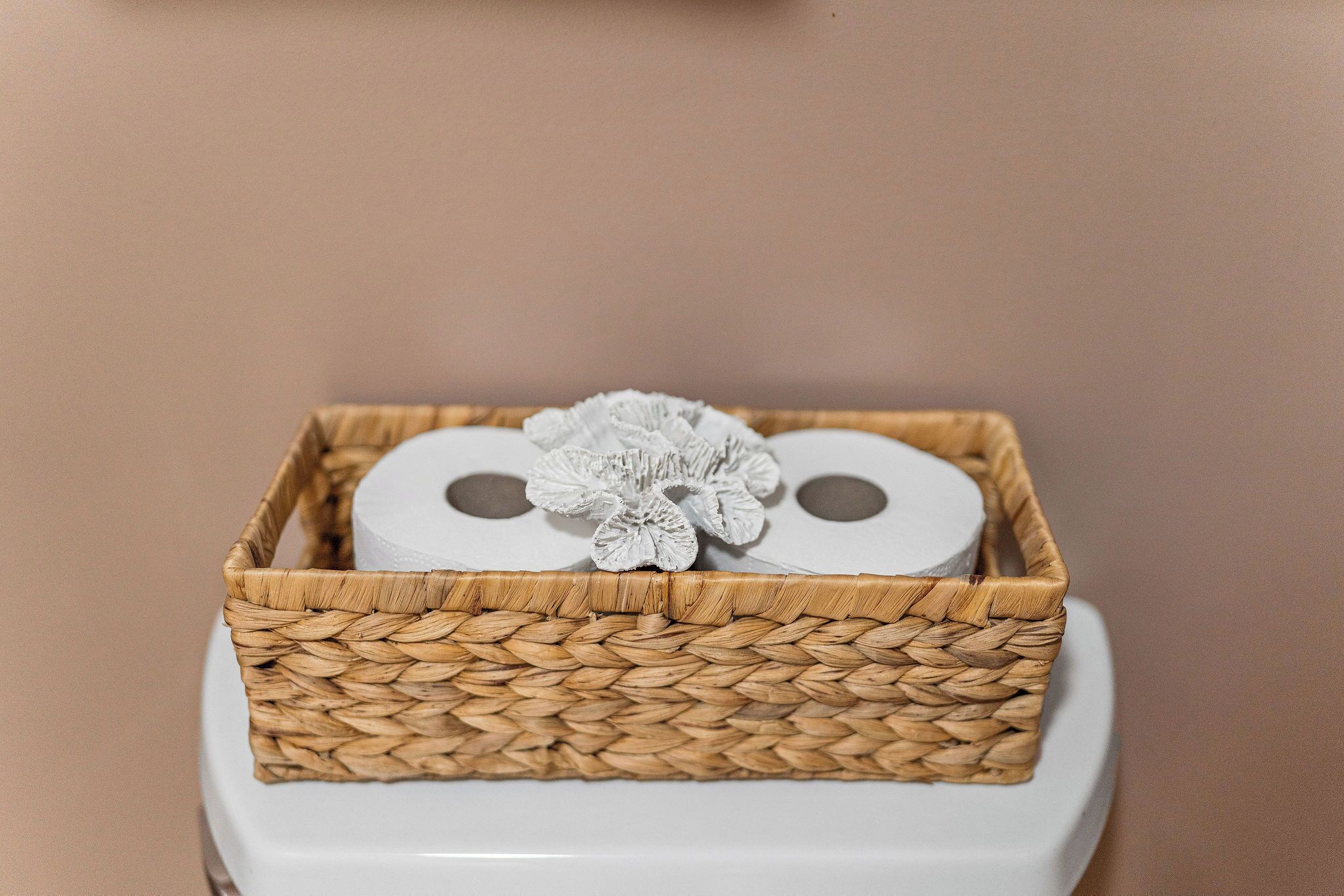 A toilet paper roll in a woven basket on a toilet.