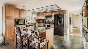 A modern kitchen with wooden cabinets, a central island with bar stools, stainless steel appliances, and a large window providing natural light.