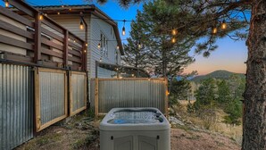 A hot tub in a backyard with a wooden fence, string lights, and a house in the background.