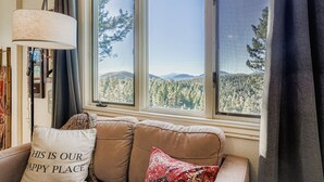 A cozy living room with a large window offering a view of a forest and mountains.