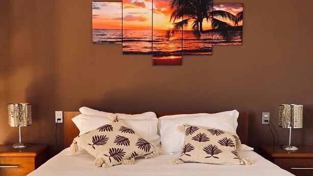 A hotel room with a large bed, two nightstands, and a multi-panel sunset artwork on the wall. - B&B Lary (Pescara)