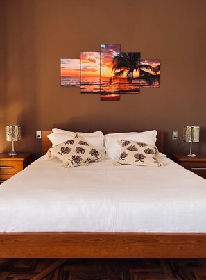 Une chambre d’hôtel avec un grand lit, deux tables de chevet et une œuvre d’art murale représentant un coucher de soleil, composée de plusieurs panneaux.
