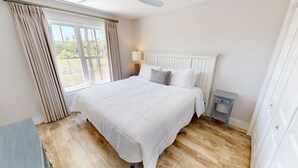 Quarto com uma cama grande, mesa de cabeceira, abajur e vista para o exterior pela janela.