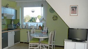 Een kleine keuken met een eettafel, stoelen, een televisie en een raam met uitzicht.