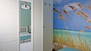 Een slaapkamer met een bed, een inloopkast, een wandplank met decoratie, en een muurschildering met strandthema.