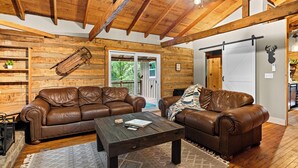 Un interior rústico con vigas de madera, sofás de cuero, una mesa de centro de madera y un portón corredizo que da a un espacio exterior.