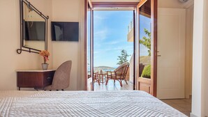 Een slaapkamer met een groot bed, een bureau met stoel, een televisie en een balkon met tafel en stoelen.