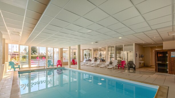 Une piscine avec des chaises longues et un mur en verre.