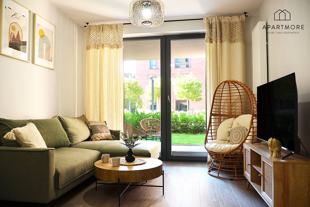 A living room with a sofa, a round coffee table, a wicker chair, a television, and a view of the outside.