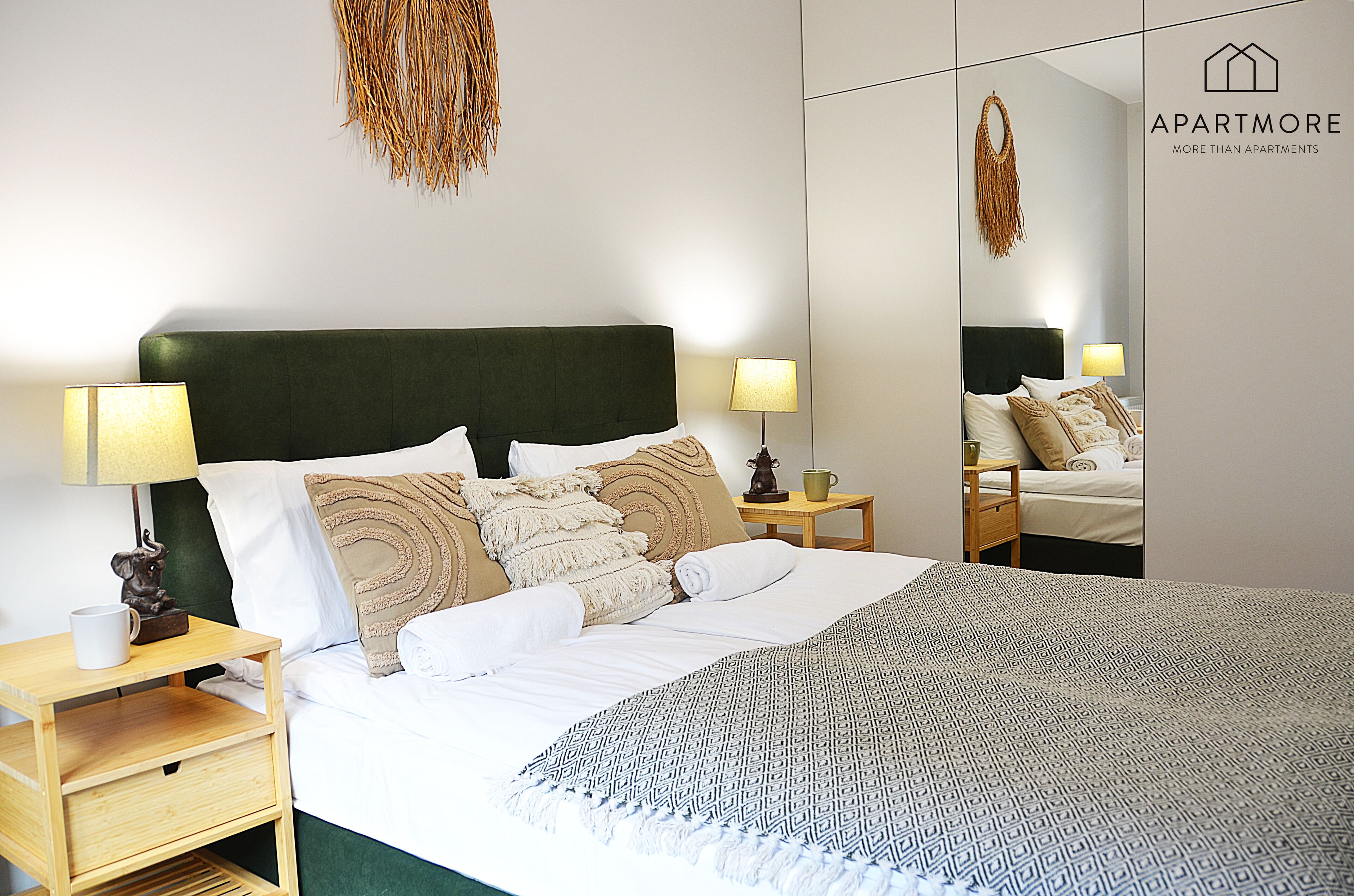 Habitación de hotel ordenada con una cama grande, dos mesitas de noche, un espejo y un letrero en la pared.