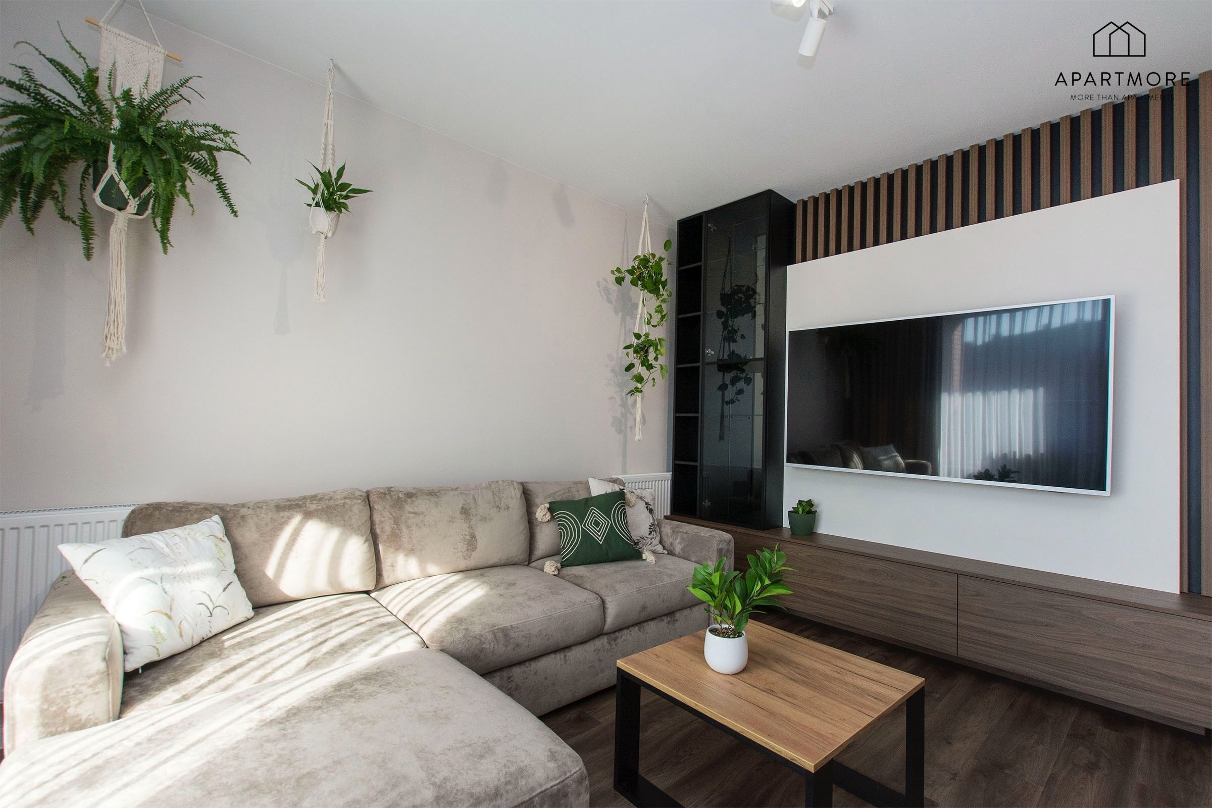 A modern living room with a sectional sofa, a coffee table, and a large flat-screen TV mounted on the wall.