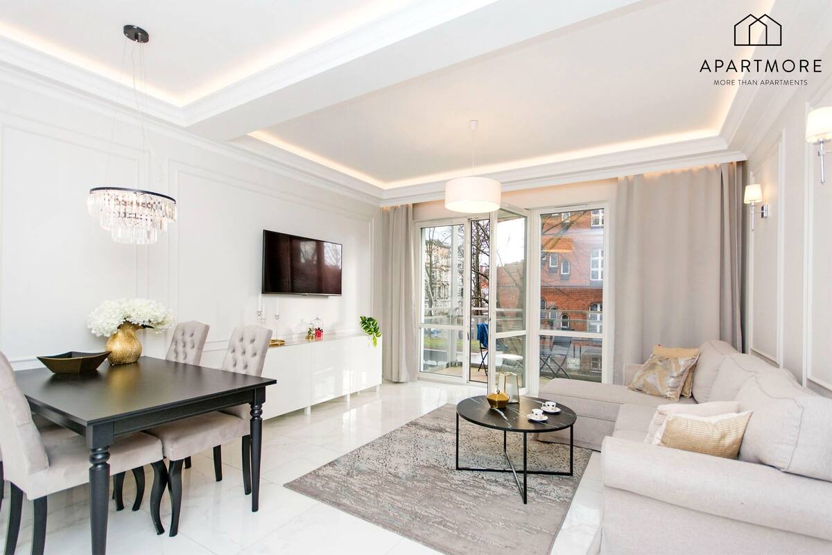A modern living room with a dining area, a sofa, a TV, and a chandelier.