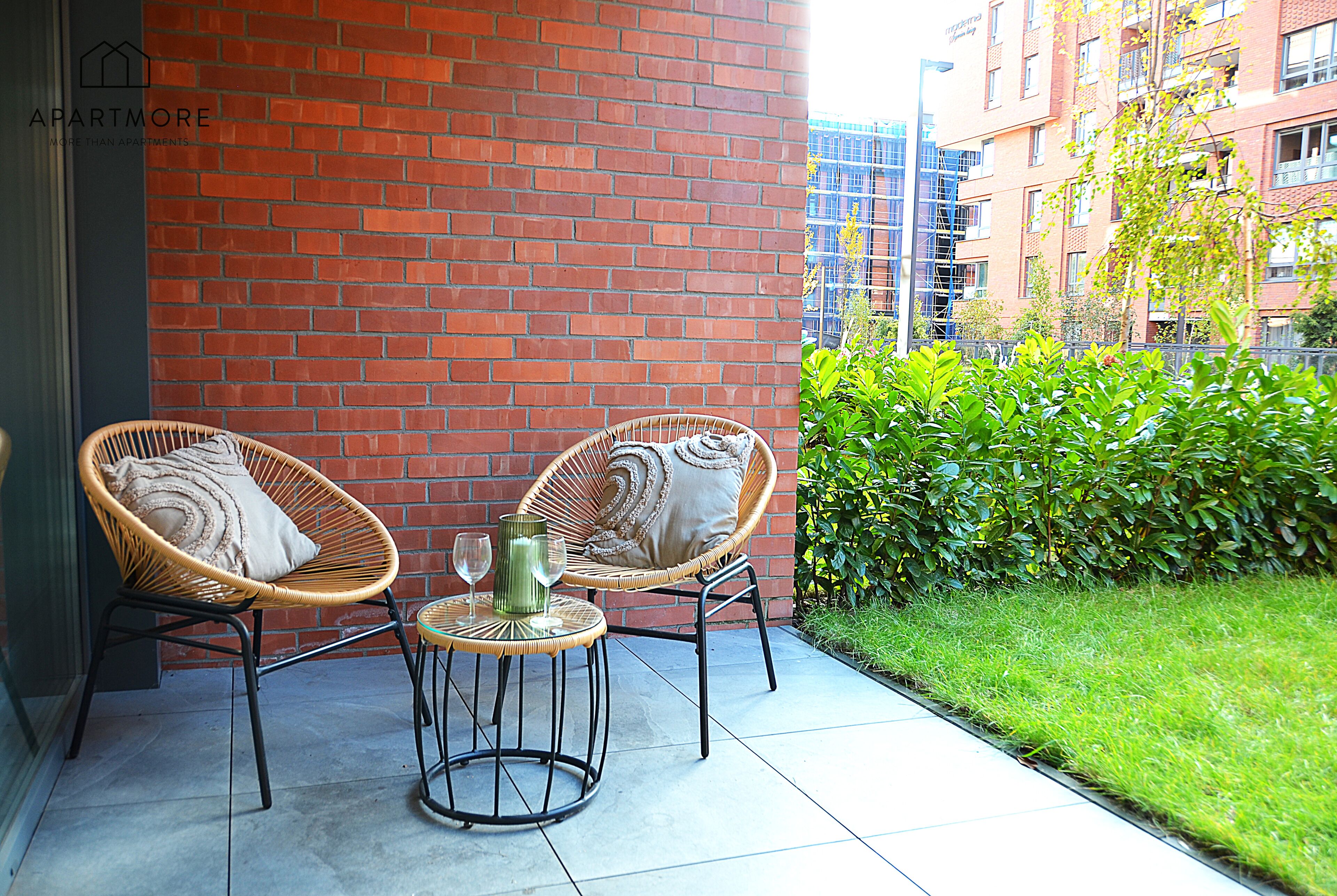 A patio with two wicker chairs, a small round table, and a decorative vase.