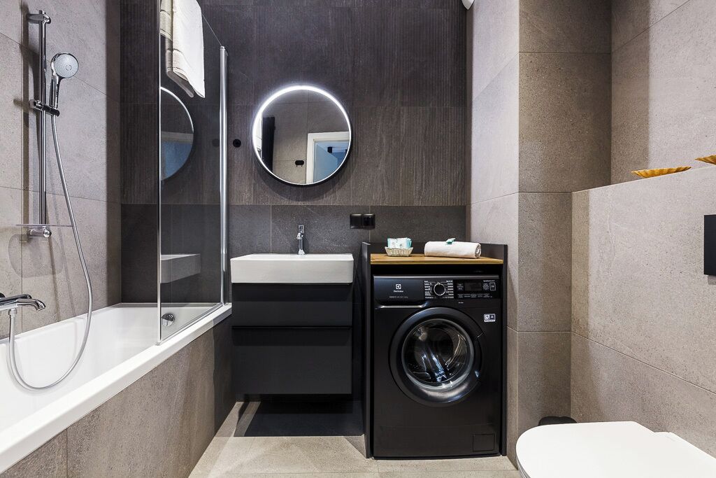 A modern bathroom with a glass-enclosed shower, a sink, a mirror, and a front-loading washing machine.