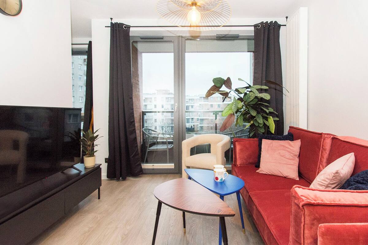 A living room with a sofa, a coffee table, a TV, and a balcony with a plant.