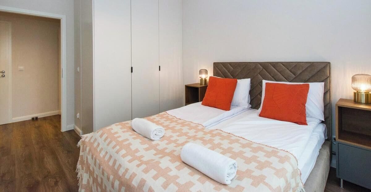 A hotel room with a bed, two bedside tables, a wardrobe, and a door.