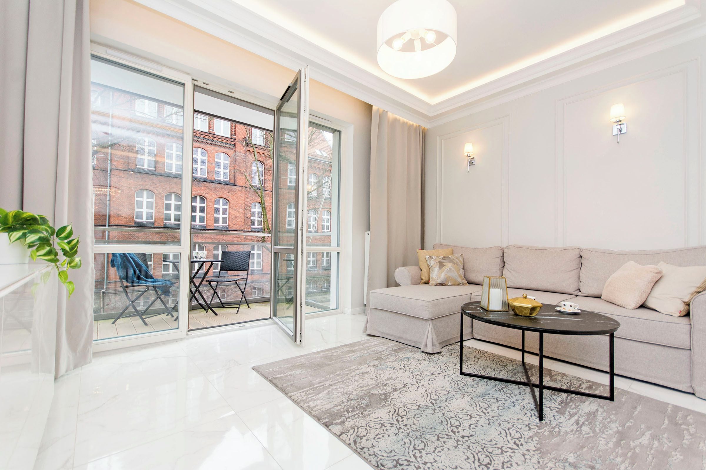 A modern living room with a sofa, a coffee table, and a view of a red brick building through large windows.