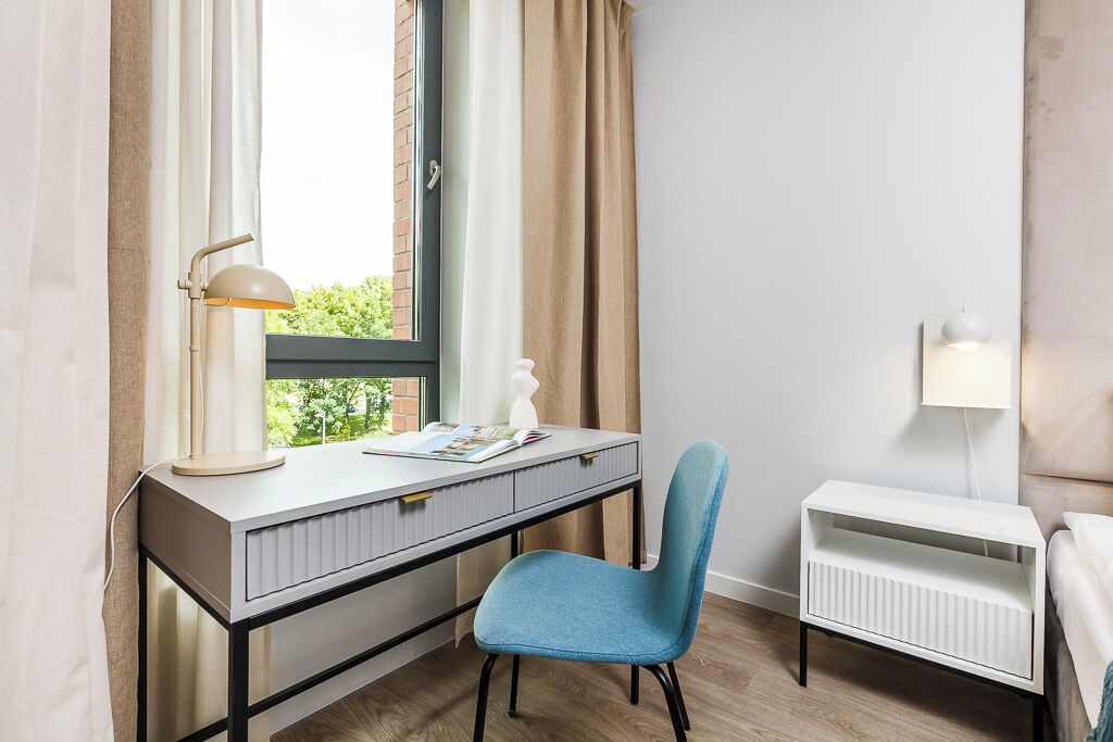 A modern bedroom with a desk, chair, radiator, and window with curtains.