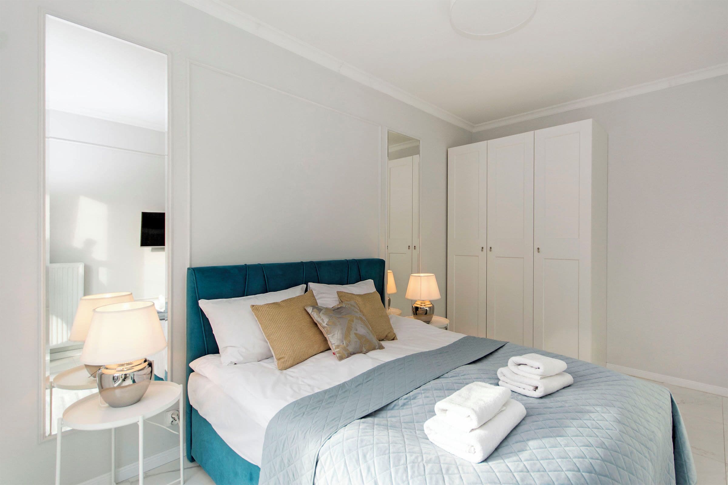 A hotel room with a bed, bedside tables, lamps, a blue headboard, and a wardrobe.