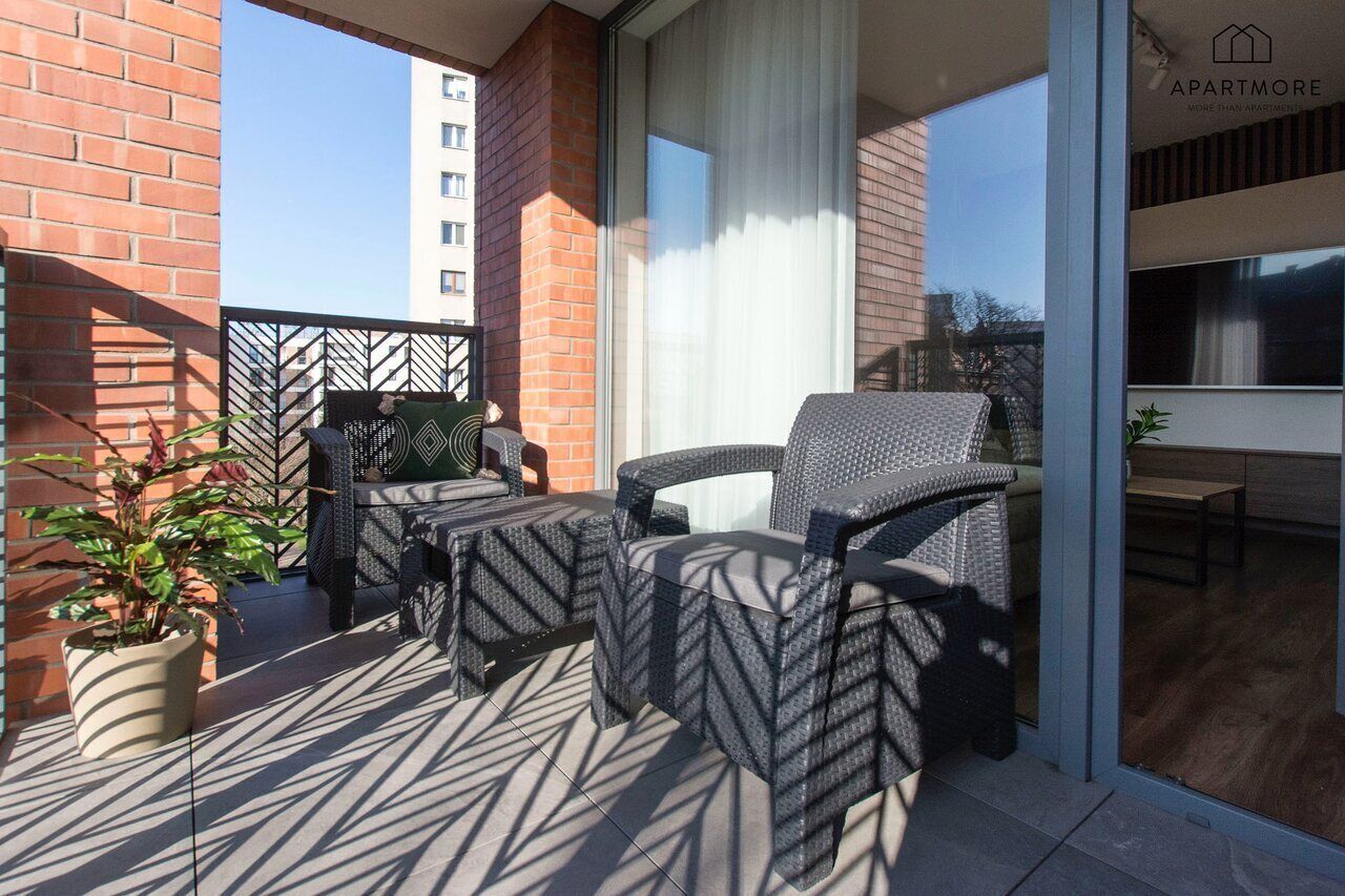 A balcony with wicker furniture, a potted plant, and a view of a building.