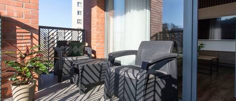 A balcony with wicker furniture, a potted plant, and a view of a building.