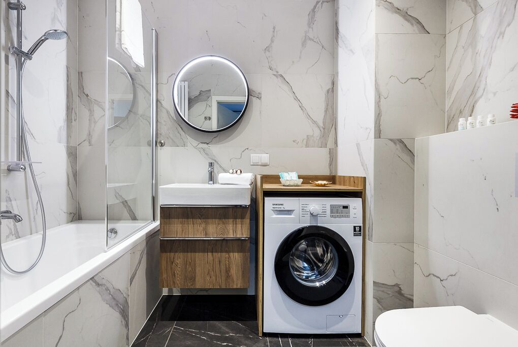 Une salle de bain moderne avec une douche à parois de verre, un miroir rond, un lavabo encastré et un lave-linge à chargement frontal.