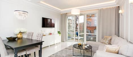 Una sala de estar moderna con comedor, sofá, televisor y candelabro.