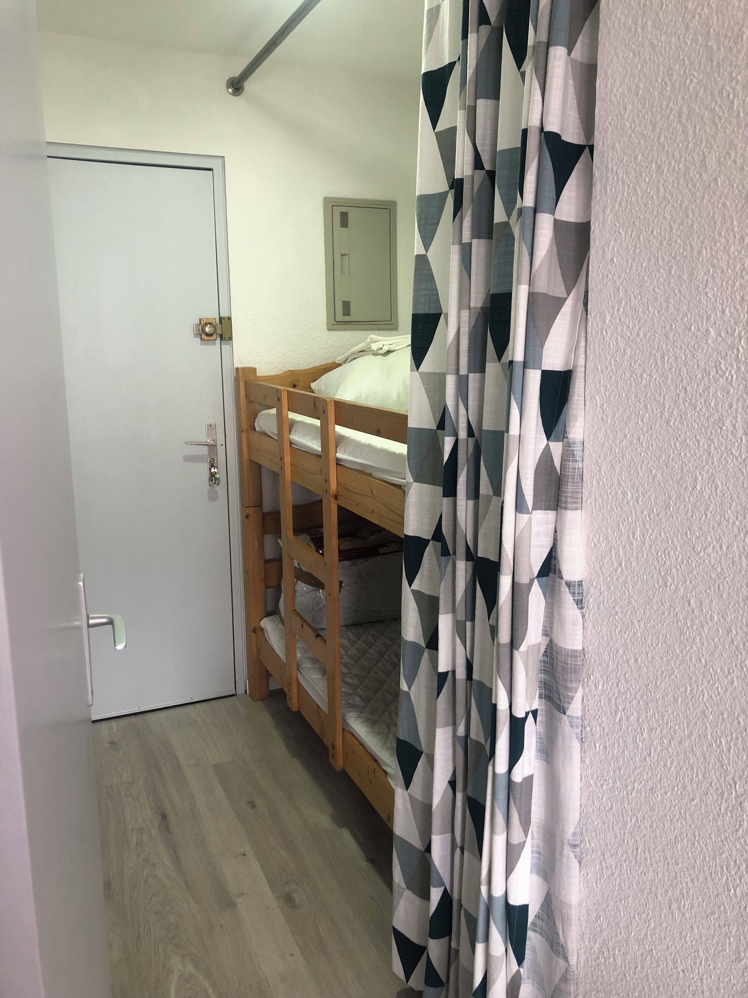 Une pièce avec un lit superposé, une porte, un climatiseur fixé au mur et un rideau à motifs.