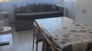 Et moderne værelse med spisebord, stole, sofa med hynder, en radiator og et vindue med lette gardiner.