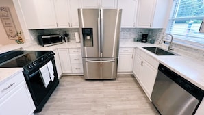 Una cocina moderna con armarios blancos, electrodomésticos de acero inoxidable, microondas, cafetera y lavavajillas.