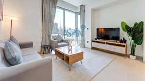 Ein modernes Wohnzimmer mit Sofa, Couchtisch, Fernseher und einem großen Fenster mit Vorhängen.