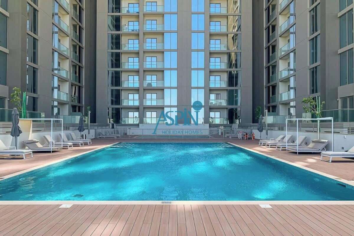 Un hotel moderno con piscina central, varios balcones y vista despejada de la fachada.