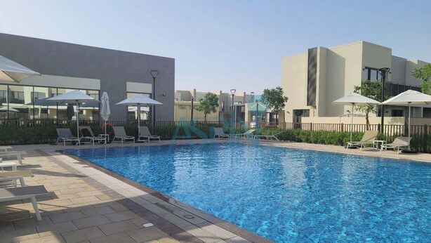 A swimming pool with lounge chairs and umbrellas, surrounded by modern buildings.